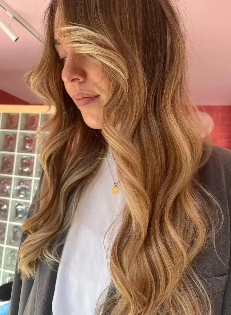 Vrouw met lang, golvend haar in warme balayage kleuren met lichtere highlights aan de voorkant.