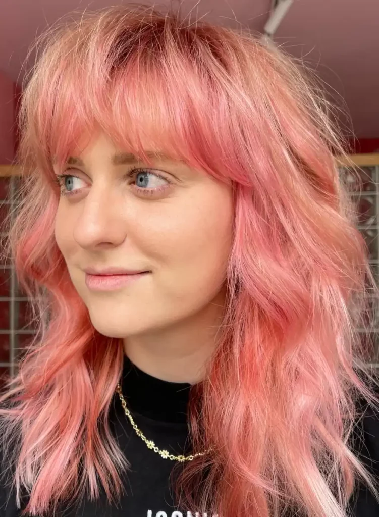 Vrouw met pastelroze creative color-haarkleur en losse golven kijkt opzij.