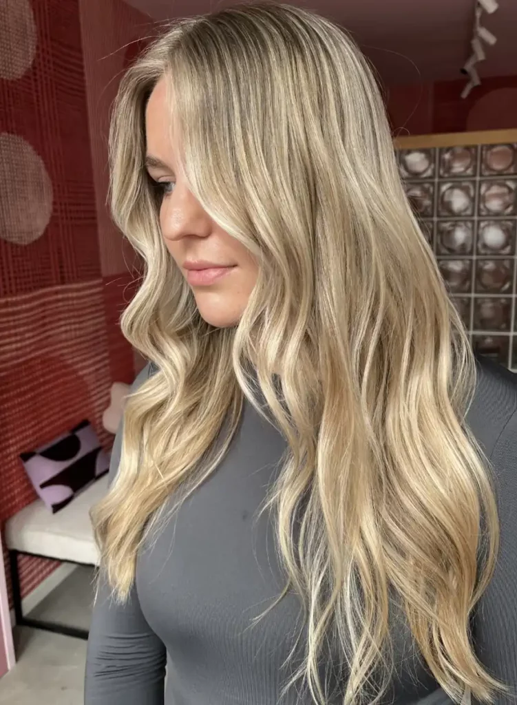 Vrouw met lang, golvend blond haar met subtiele highlights in een kapsalon.