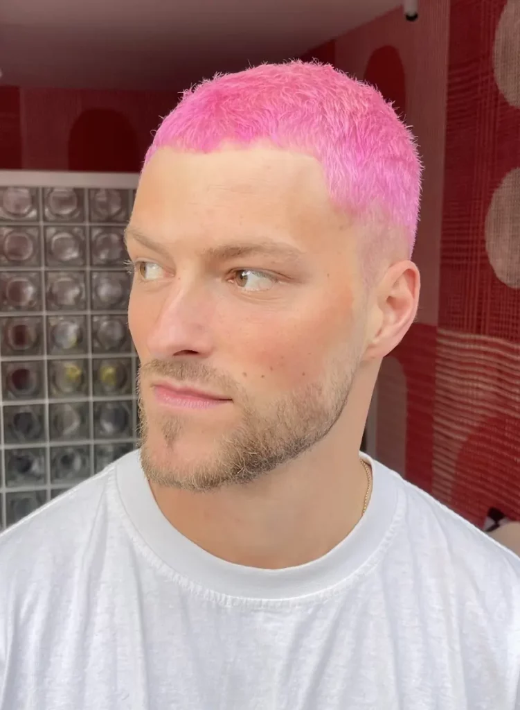 Man met kort, felroze haar geverfd in de stijl van Colorbar Twiggy James, kijkt opzij in een modern ingerichte ruimte.