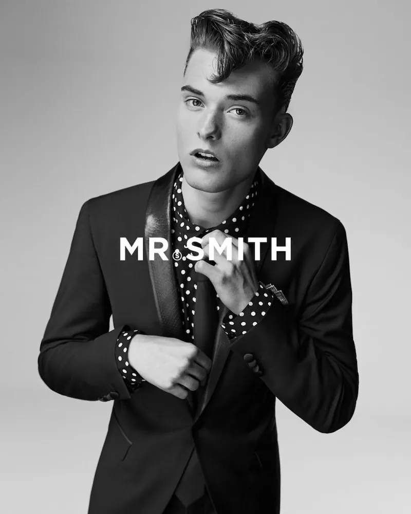 Jonge man in een zwart pak en polkadot overhemd poseert voor de camera met de tekst "MR. SMITH" op de voorgrond.