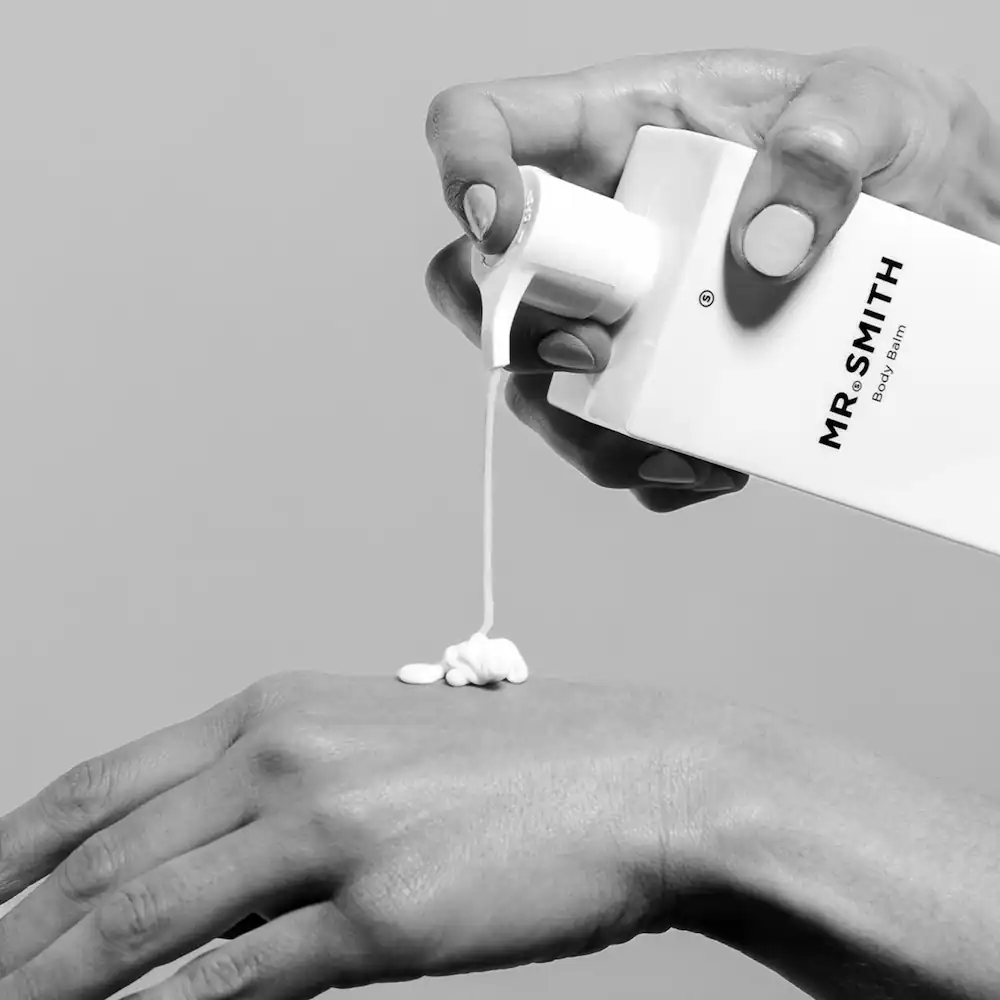 Zwarte-wit afbeelding van een hand die Mr. Smith body balm op de rug van een andere hand aanbrengt.